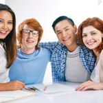 Company of smiling groupmates embracing and looking at camera