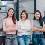 Group of Asia young creative people in smart casual wear smiling and arms crossed in creative office workplace. Diverse Asian male and female stand together at startup. Coworker teamwork concept.