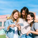 Group of young Asian Women selfie themselves with a phone in a pastel town after shopping. Young women group do outdoor activity under the blue sky. Outdoor activity after shopping concept.